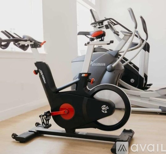 A stationary exercise bike with a black and red seat and handlebars is in a room.