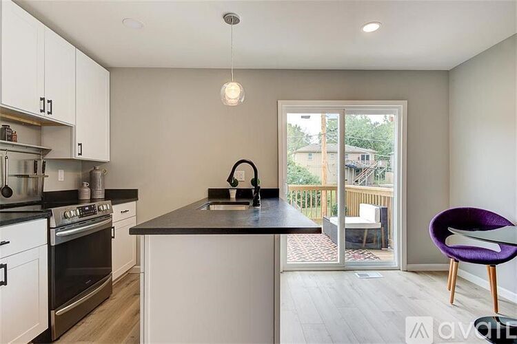A kitchen with white cabinets and a black countertop with a purple chair.