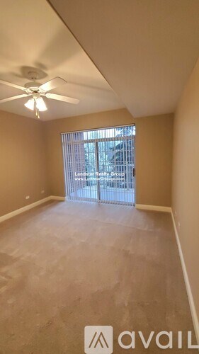 A room with a ceiling fan and a window overlooking a parking lot.