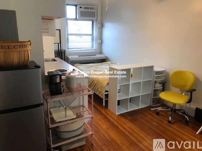A room with a refrigerator, a bed, and a yellow chair.