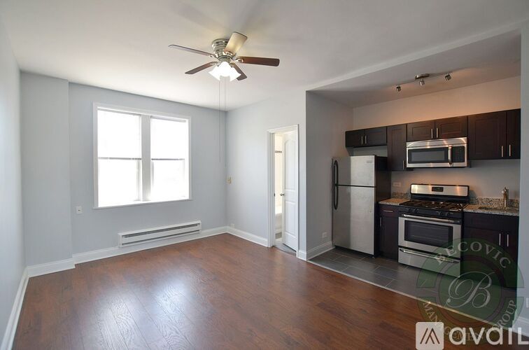 A living room with a wood floor and a kitchen area in the background.