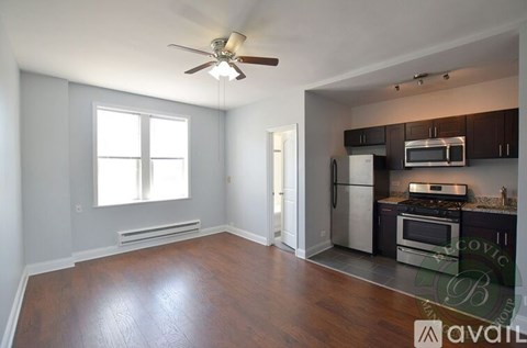A living room with a wood floor and a kitchen area in the background.