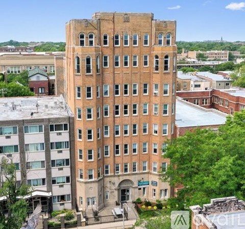 A tall red brick building with many windows is in the foreground of a city scene.