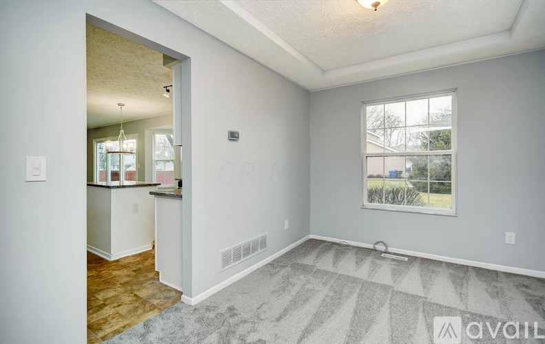 A room with a grey carpet and a window showing a view of trees and houses outside.