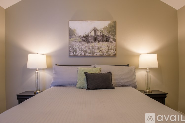 A bedroom with a bed, two lamps, and a painting on the wall.