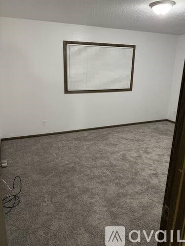 A room with a carpeted floor and a window with blinds.