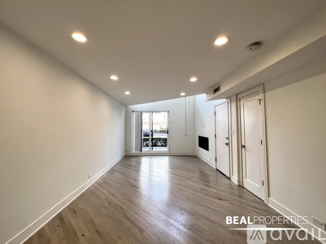 A spacious room with wooden flooring and white walls, leading to a balcony.