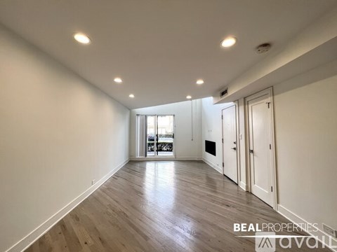 A spacious room with wooden flooring and white walls, leading to a balcony.