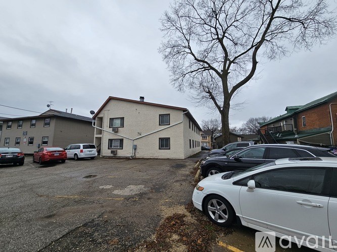A white car is parked in a lot with other cars and a building in the background.