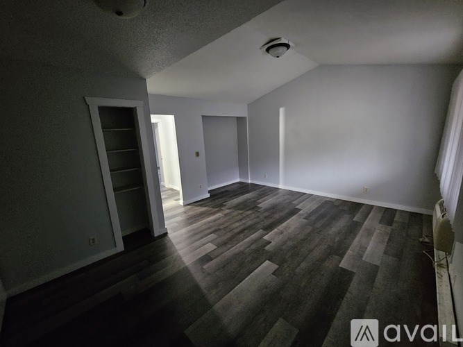 A room with wooden flooring and white walls, with a door and a window.