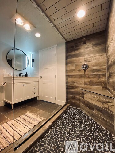 A bathroom with a mirror, wooden wall, and a black and white rug.