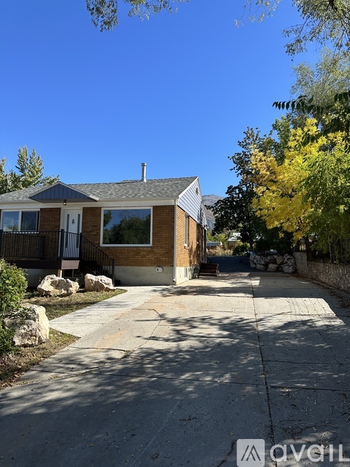 A house with a brown brick exterior and a white door is surrounded by a sidewalk and trees.