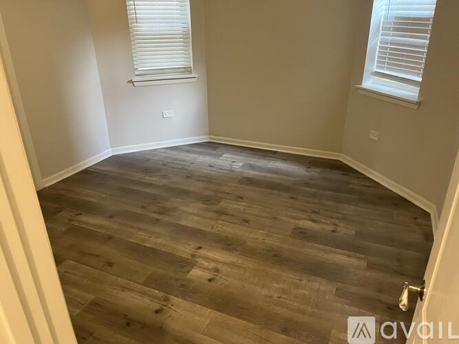 A room with wooden flooring and two windows with blinds.