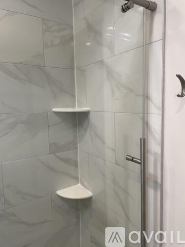 A white shower stall with a glass door and a white shelf.