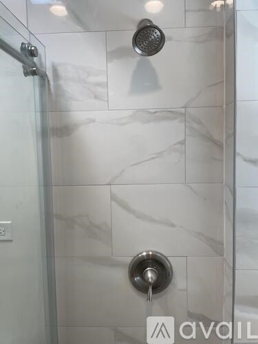 A shower with a glass door and a marble wall.