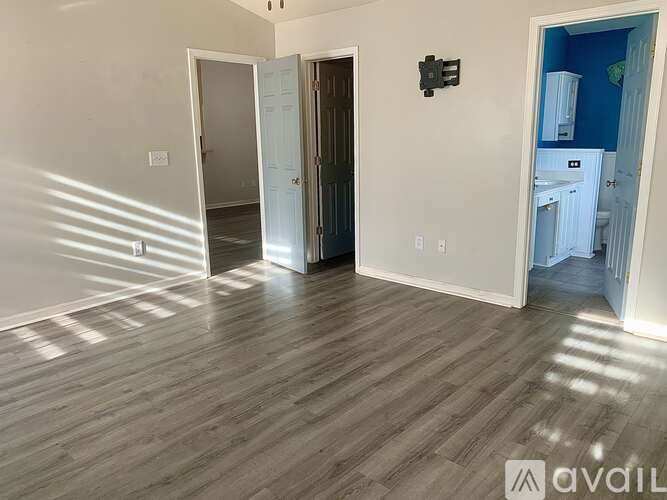 A room with light wood flooring and white walls, with a door open to another room.