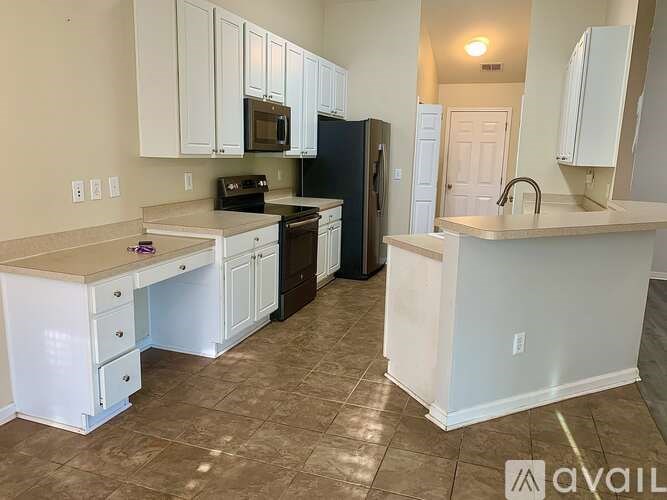 A kitchen with white cabinets and brown flooring.