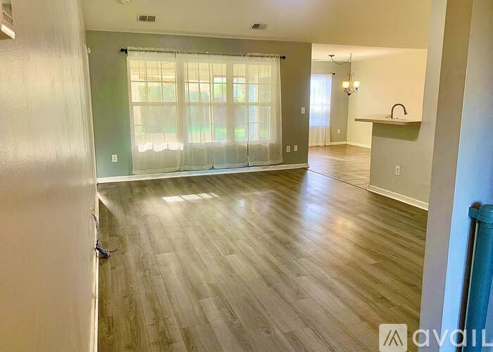 A spacious living room with wood flooring and a large window with curtains.