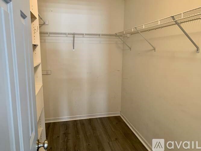 A small, empty room with a white door and a white wall with a shelf and a rack.