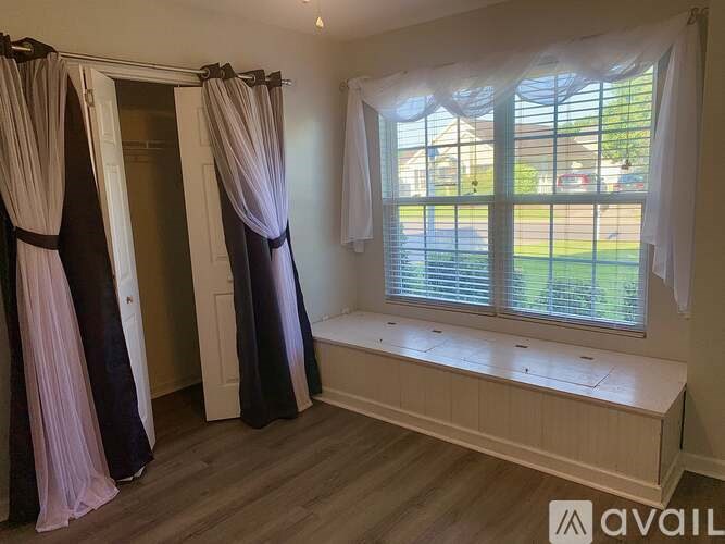A room with a window and a bench with curtains hanging on the windows.