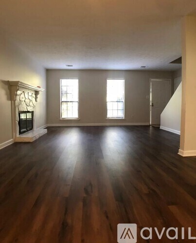A spacious room with wooden floors and three windows.