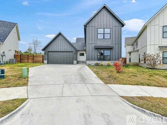 A modern house with a grey garage door is surrounded by a well-maintained lawn and other houses.