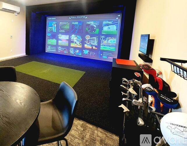 A room with a screen displaying video games and a table and chairs in front of it.