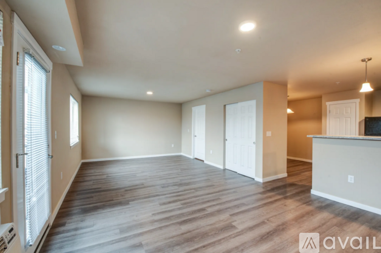 A spacious living room with wooden flooring and a kitchen area in the background.