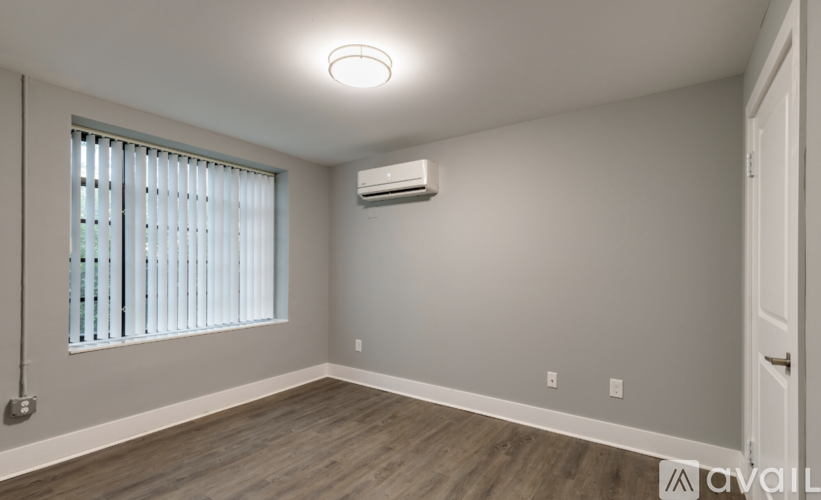 A room with a window, wooden floor, and an air conditioner.