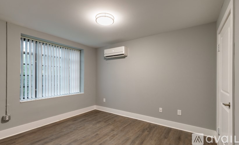 A room with a window, wooden floor, and an air conditioner.
