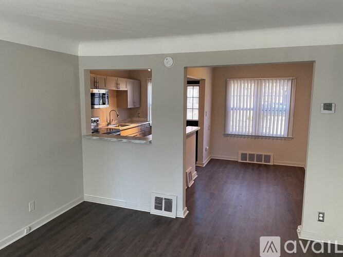 A living room with a kitchen in the background and a window with blinds.