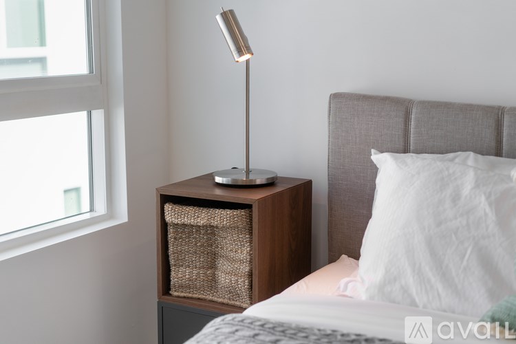 A bedroom with a bed, a nightstand with a lamp, and a window.