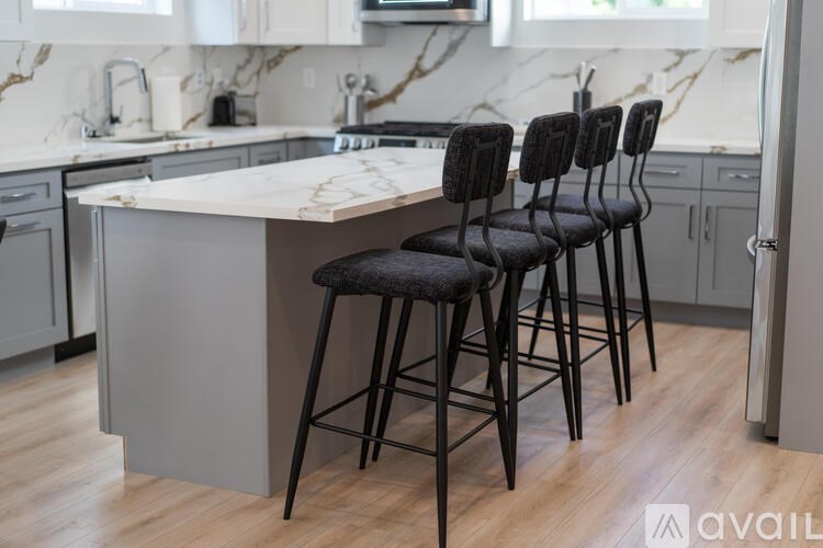 A kitchen with a marble countertop and a set of four black barstools.