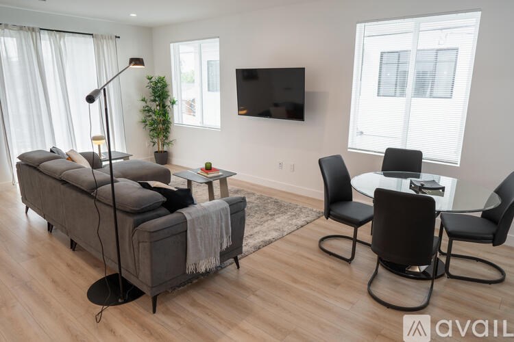 A living room with a grey sofa, a black chair, a small table, and a television mounted on the wall.