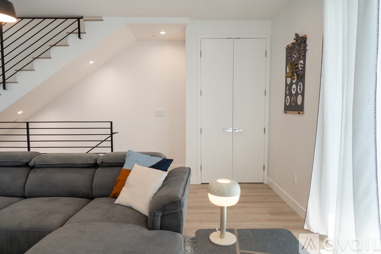 A grey couch with a pillow and a lamp on a grey rug in a room with a white door and a white wall.