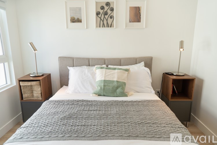 A bed with a grey headboard and a white pillow with green stripes is in the center of the image.