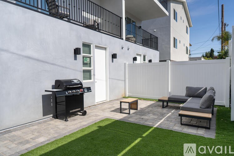 A modern outdoor patio area with a grill, seating, and a white fence.