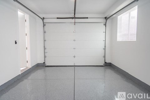 A spacious room with a white door and a window on the right side.