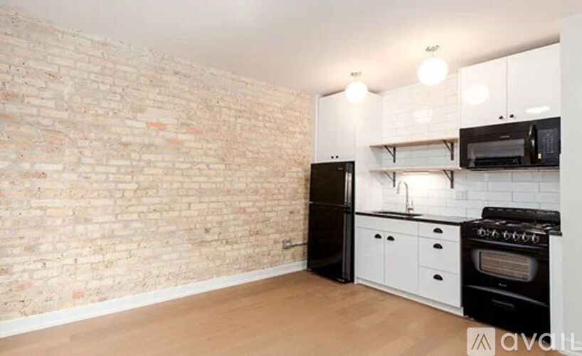 A kitchen with a black refrigerator, white cabinets, and a brick wall.