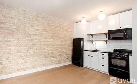 A kitchen with a black refrigerator, white cabinets, and a brick wall.