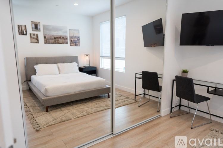 A bedroom with a bed, two chairs, and a television mounted on the wall.