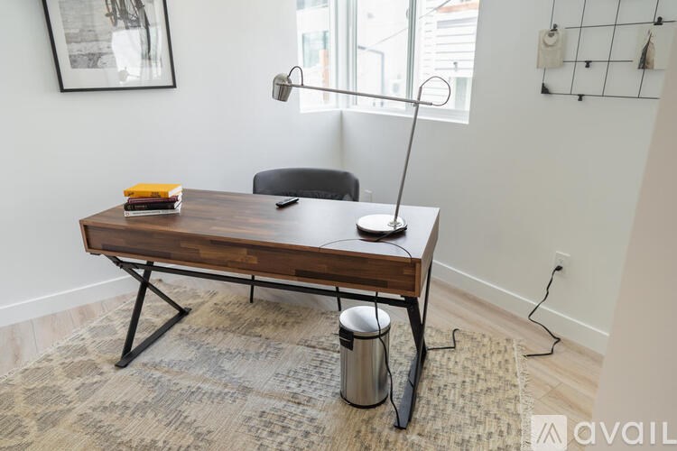 A wooden desk with a black chair and a silver trash can in front of it.