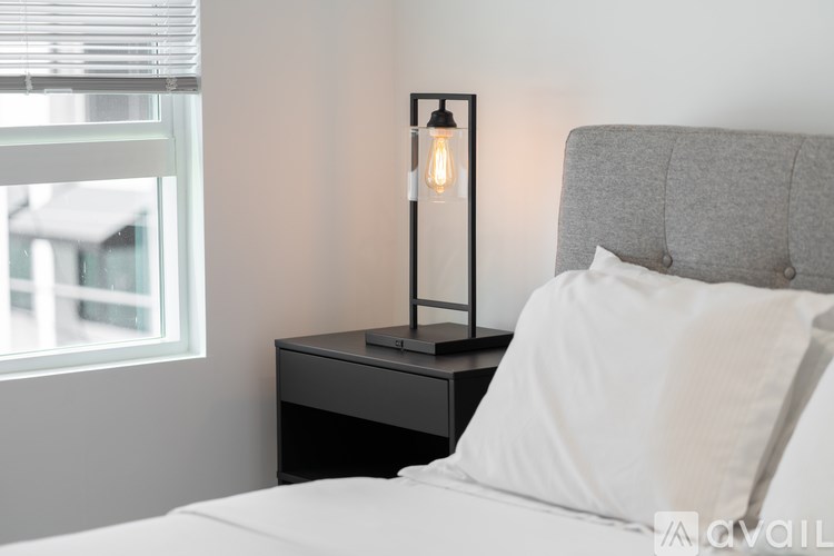 A bedroom with a bed, nightstand, and a lit lamp.