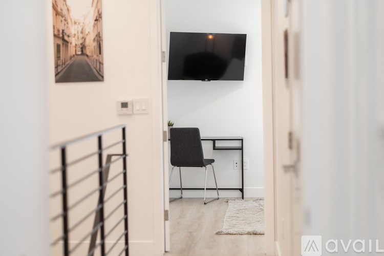 A black chair is in front of a white desk with a black screen on the wall.