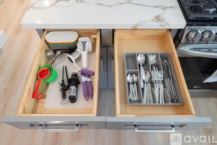 A drawer with utensils and a spice container is open.