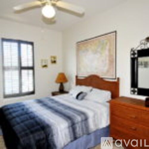 A bedroom with a bed, a ceiling fan, a nightstand with a lamp, and a painting on the wall.