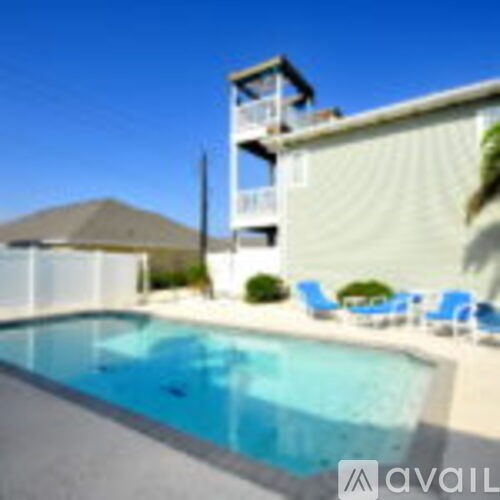 A swimming pool in front of a house with a deck and chairs.