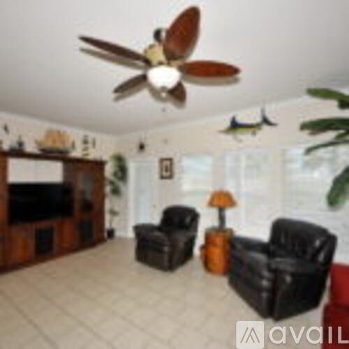 A living room with a ceiling fan and two black leather chairs.