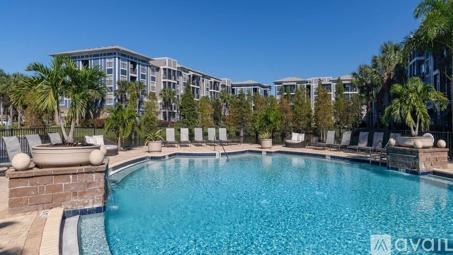 A pool surrounded by lounge chairs and palm trees with apartment buildings in the background.