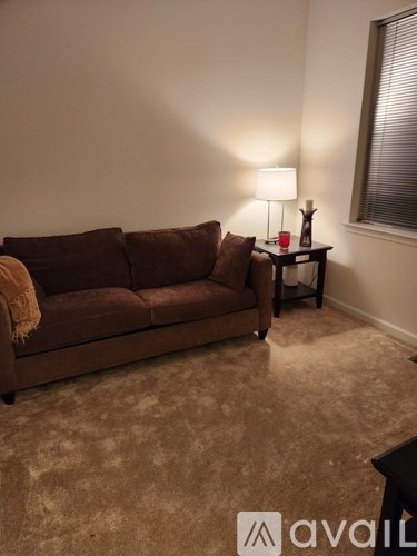 A brown couch sits in a living room with a lamp and a small table.